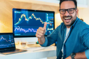 a happy man front of screen with trading charts